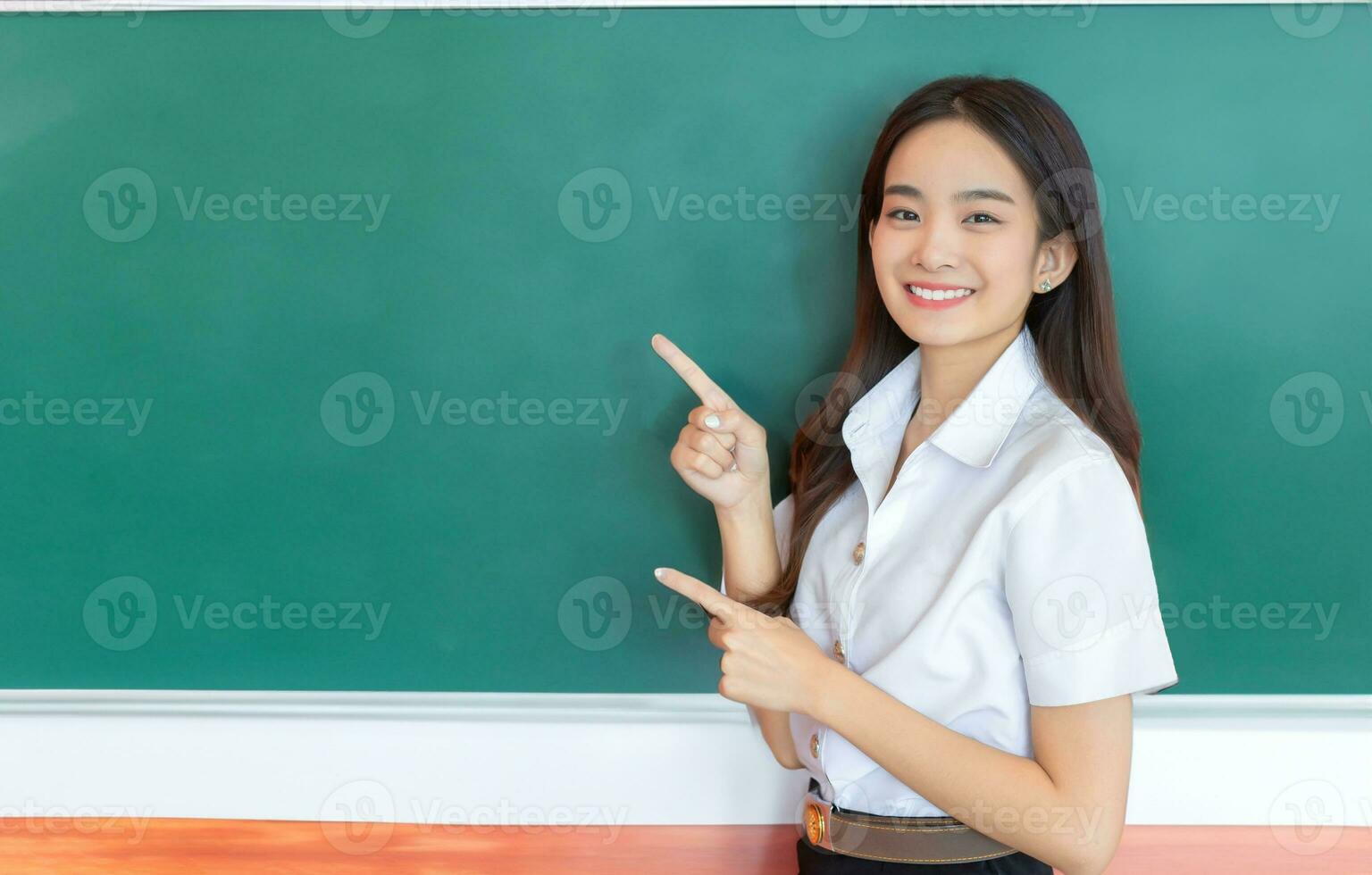 Porträt von Erwachsene thailändisch Student. schön asiatisch jung Frau Schüler im Uniform ist lächelnd zu Geschenk etwas selbstbewusst mit Tafel, Grün wie Hintergrund im Klassenzimmer beim das Universität. foto