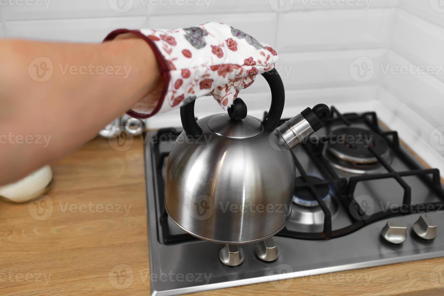 Mann Hand in Fäustlingen mit metallischem Wasserkocher in der Küche. foto