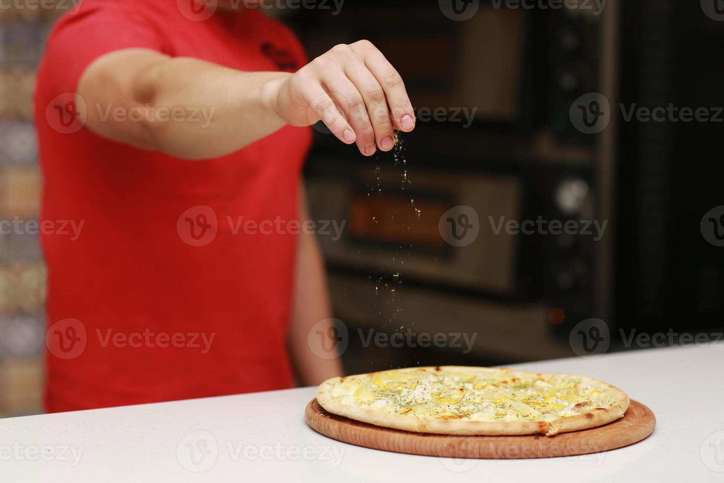 Der Koch bereitet die Pizza zu und bestreut sie mit Gewürzen. das Konzept von leckerem Essen und gesundem Essen. auf schwarzem Hintergrund für Design oder Beschriftungstext. selektiver Fokus foto