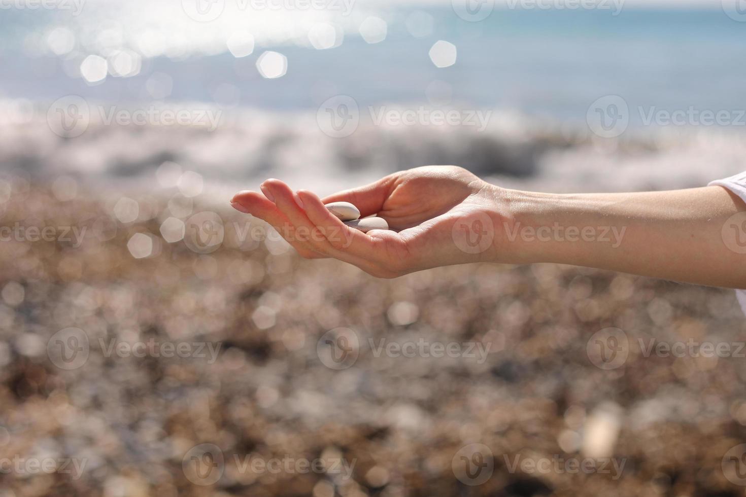 weibliche Hand, die kleine Kieselsteine in der Hand in der Nähe des blauen Meeres auf einem Strandhintergrund hält, Kieselsteine am Steinstrand aufheben, runde Kieselsteine, Sommerurlaubs-Souvenir, Strandtag, selektiver Fokus foto