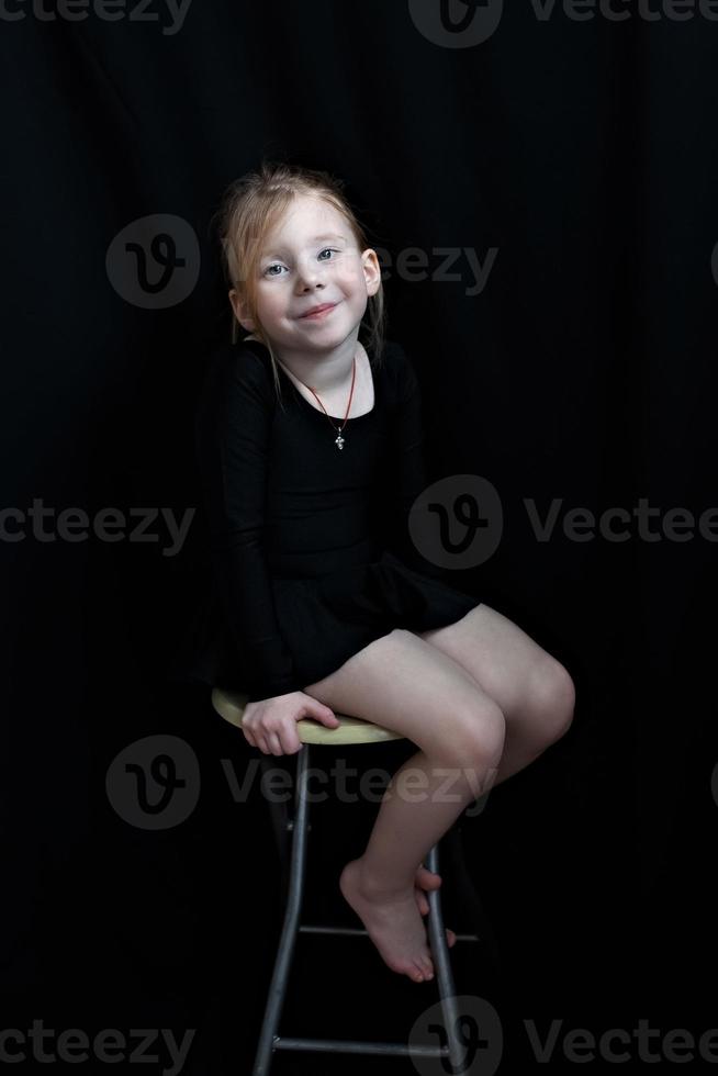 kleines Turnerin auf einem Hocker auf schwarzem Hintergrund foto