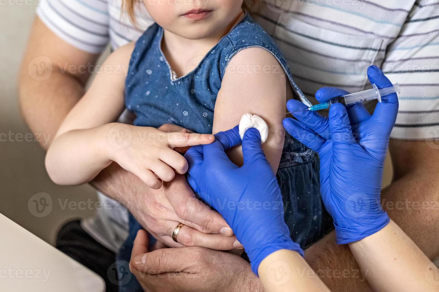 ein kleines mädchen mit ihrem vater in der arztpraxis der klinik wird gegen das coronavirus geimpft. das konzept der impfung, immunisierung, prävention gegen covid-19. foto