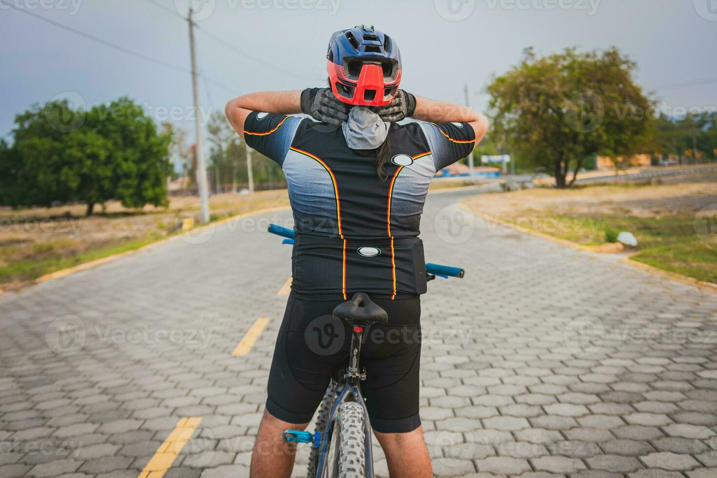 Rückseite Aussicht von ein Radfahrer mit Hals Schmerzen mit das Fahrrad. zurück Aussicht von ein Radfahrer Mann haben Hals Schmerzen während Reiten ein Fahrrad foto
