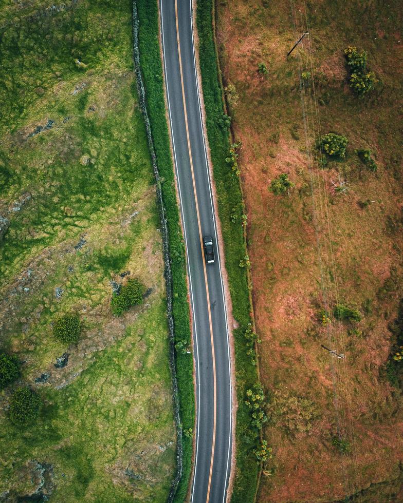 Luftaufnahme von oben auf ein Auto, das auf einer Straße zwischen Gras und trockenem Gras in Maui, Hawaii fährt foto