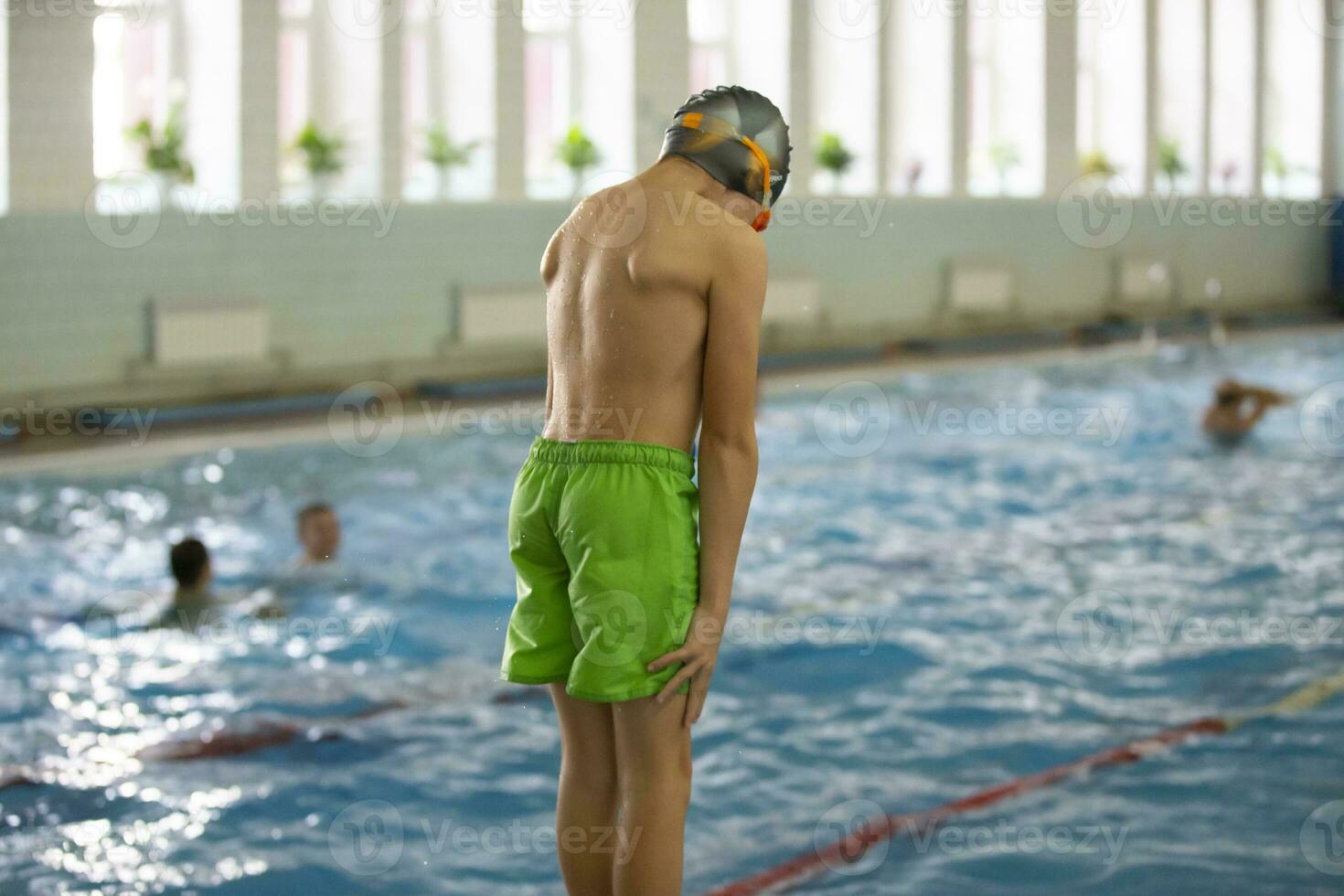 ein Junge im ein Schwimmen Deckel und Brille Tauchgänge in ein Sport Schwimmbad. foto