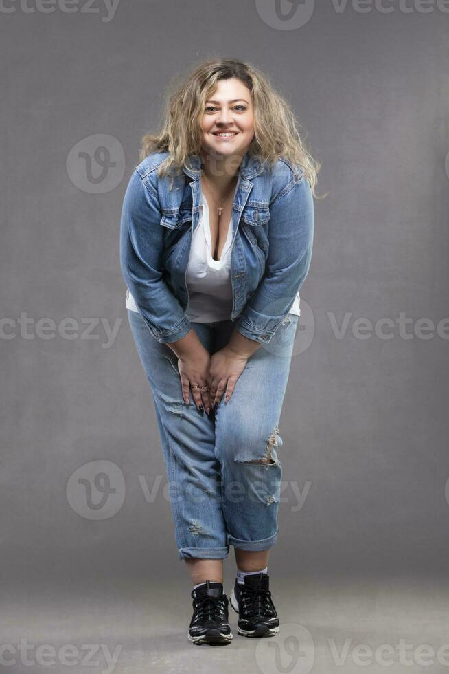 schön rundlich Frau im ein Denim passen auf ein grau Hintergrund. foto