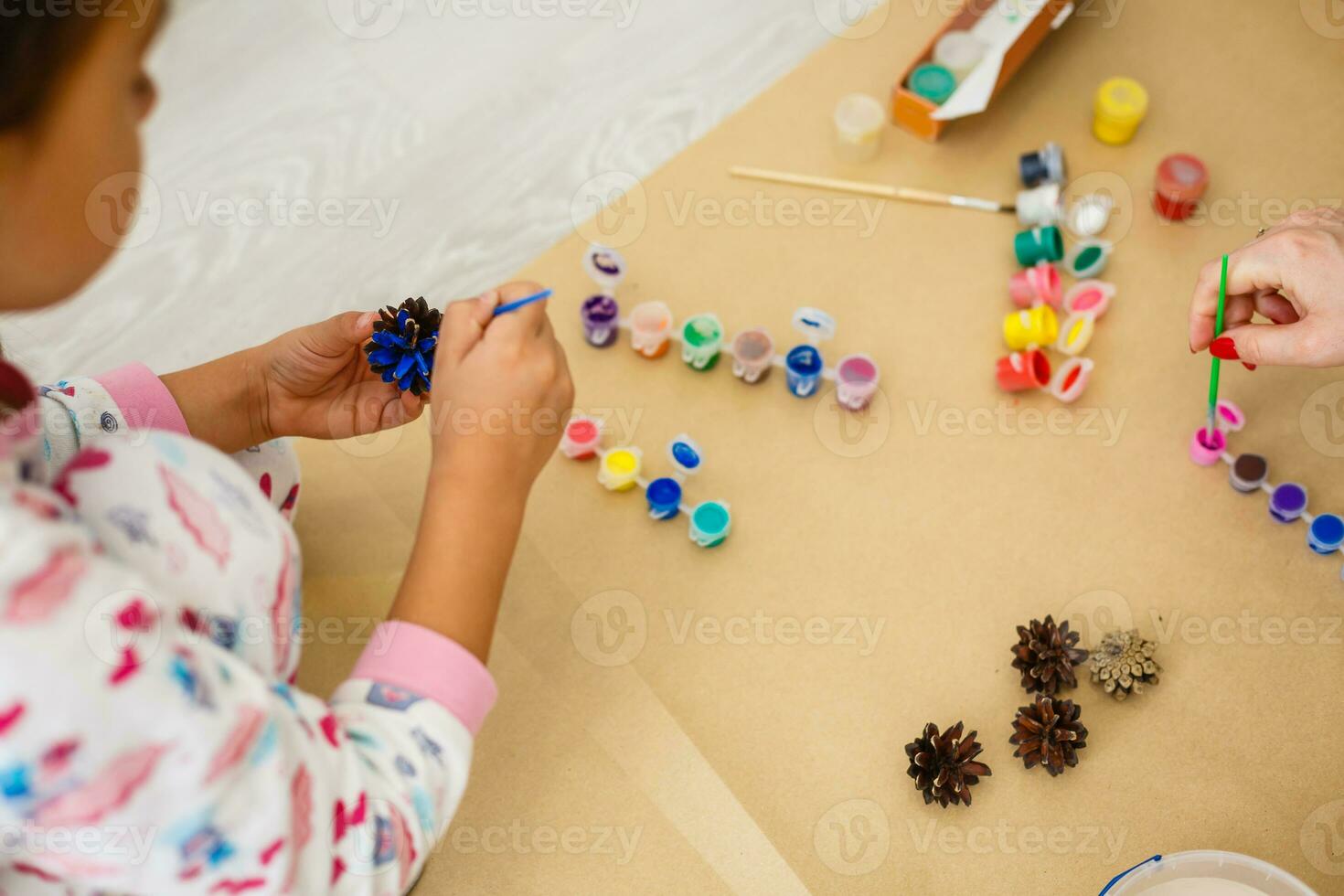 süß wenig Mädchen Färbung ein natürlich Kegel Tanne zu erstellen ein Blume, einstellen von Bürsten, malt, natürlich Herbst Materialien, erstellen Spaß und einfach mit Kinder, DIY zum Kindergarten foto
