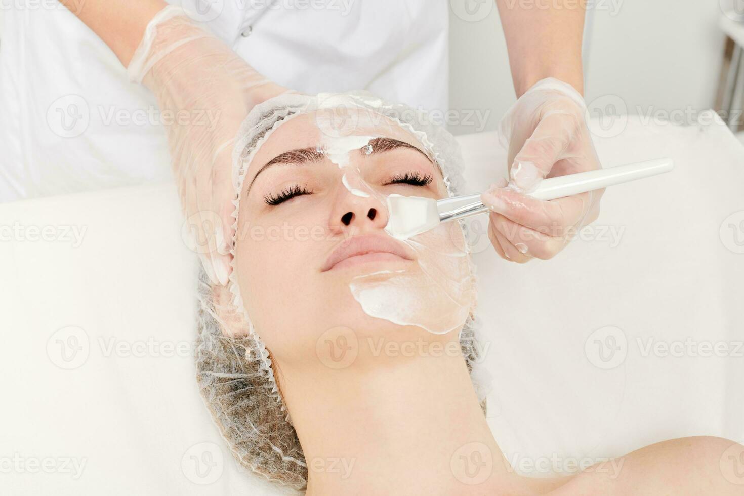 Kosmetikerin gilt Sahne Maske auf Frau Gesicht zum Verjüngung Gesicht Haut, Verfahren im Schönheit Salon foto
