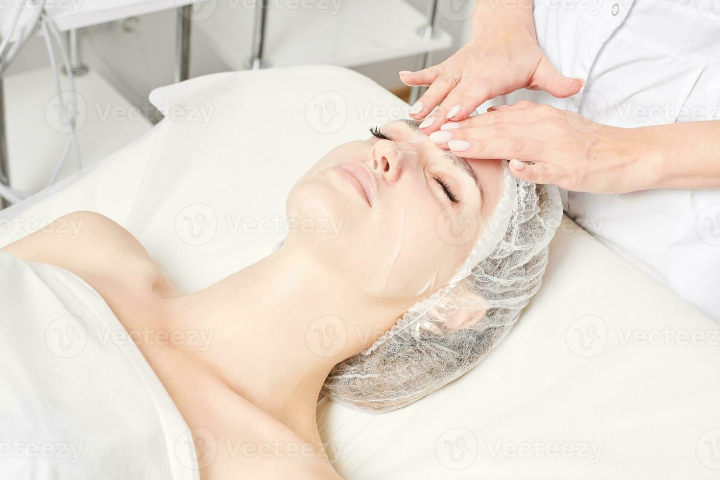 Kosmetikerin glättet Blattmaske auf dem Gesicht der Frau, um die Gesichtshaut zu rehydrieren, Verfahren im Schönheitssalon foto