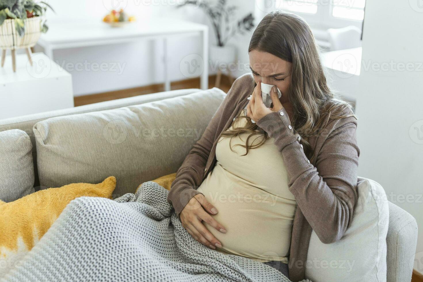 Schwangerschaft und Erkrankung. krank schwanger Frau weht Nase im Gewebe haben Fieber Sitzung auf Sofa Innen- Leiden von covid-19 foto