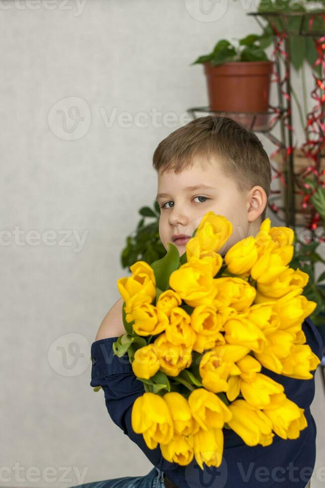 Porträt von ein jung, schön Junge. hält ein enorm Arm voll von frisch Gelb Tulpen. das Konzept von Frühling und Urlaub, März 8, International Damen Tag, foto