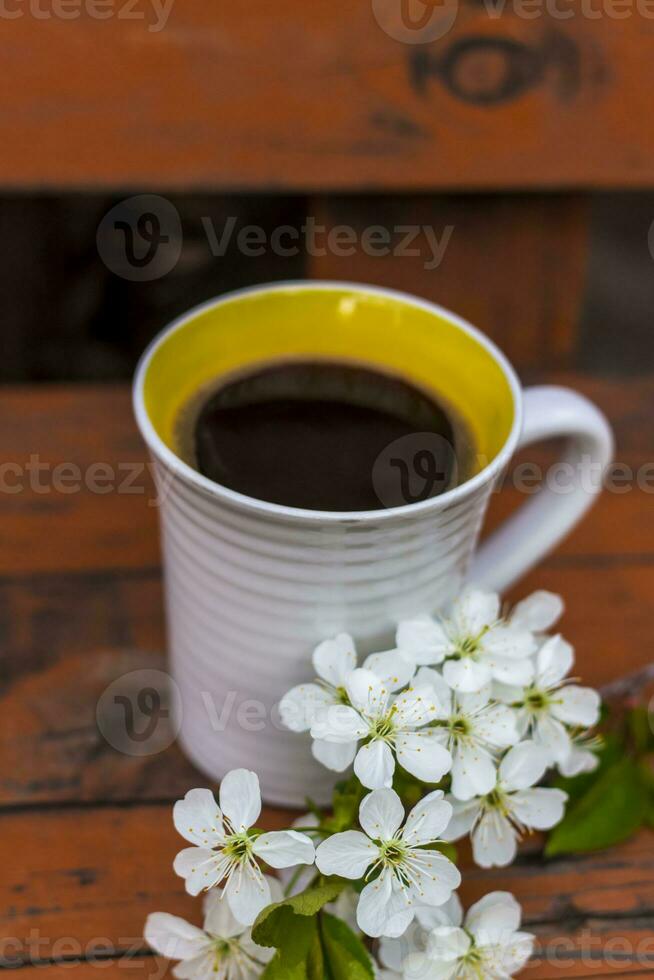 eine Tasse Kaffee auf einem dunklen, abgenutzten rustikalen Holztisch. Die Komposition ist mit einem Zweig mit weißen Blumen geschmückt. Kirschbaum blüht. selektiver Fokus. foto