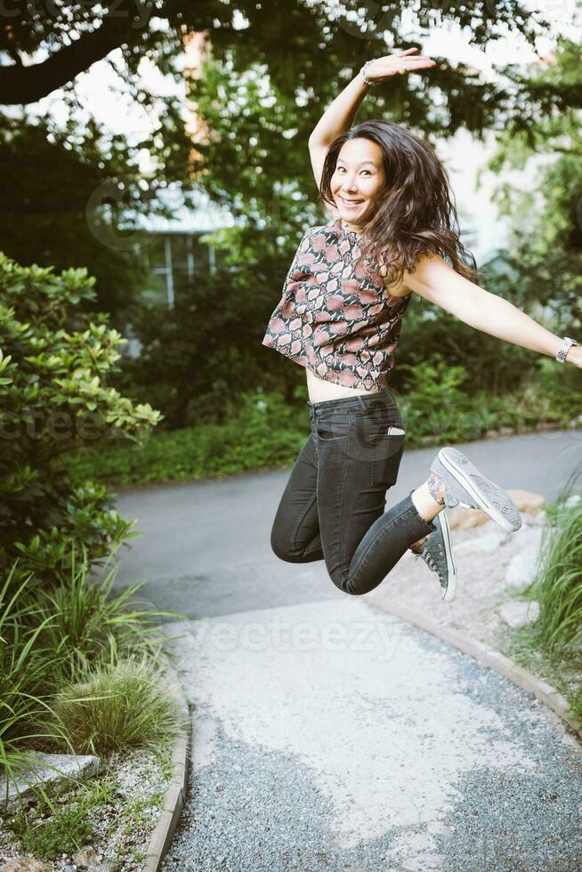 glücklich jung gemischtrassig japanisch Frau im Turnschuhe Springen im Sommer- Park foto