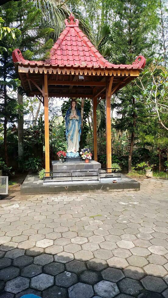 Statue von das Jungfrau Maria unter ein Überdachung mit Bäume im das Hintergrund, im das jatiningsih Maria Höhle, Jogjakarta, wo Katholiken beten, geben Vielen Dank und einreichen Anfragen zu Gott foto