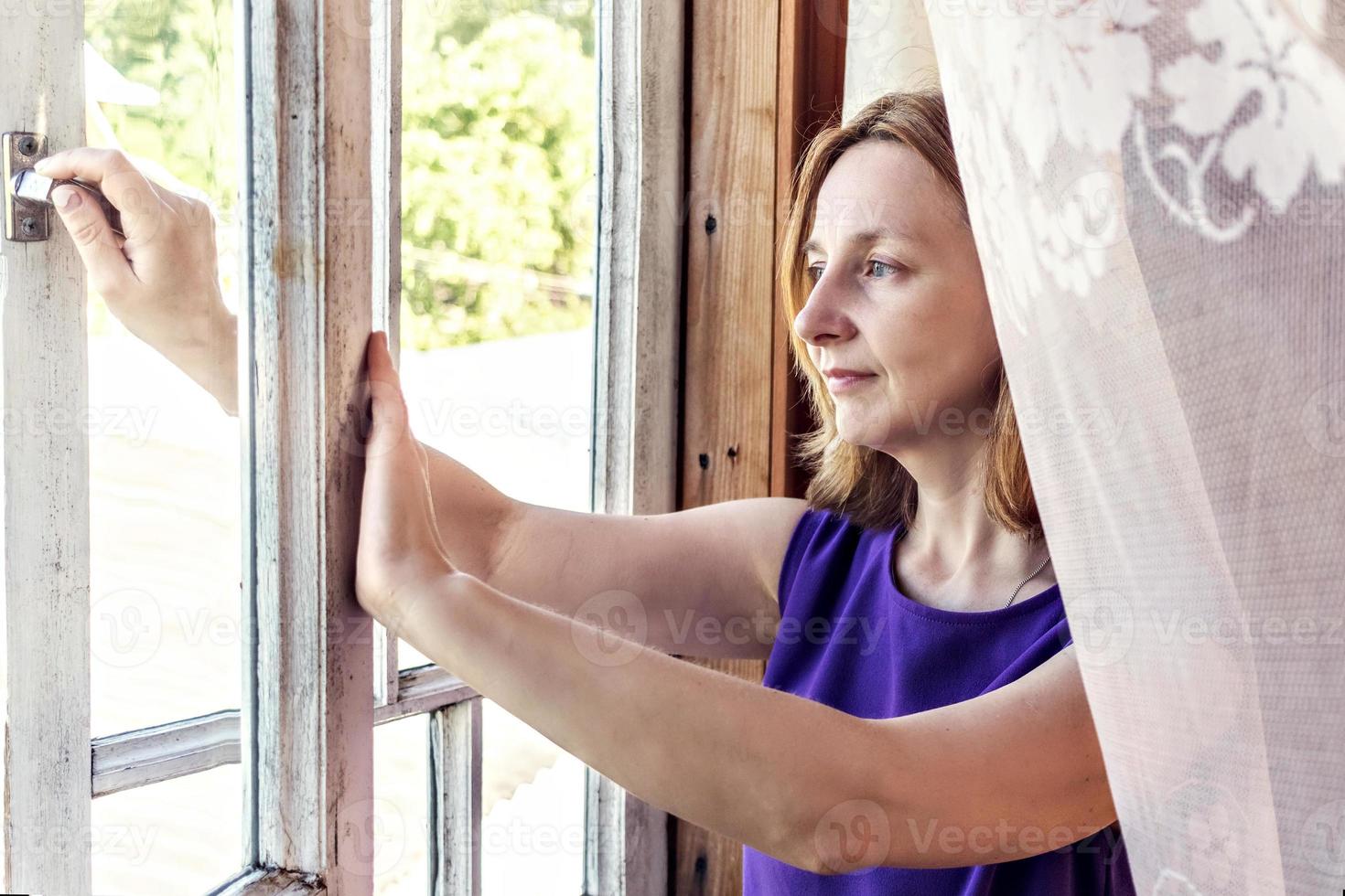 junge Frau öffnet das Fenster in ihrem Landhaus, schaut in den Garten foto