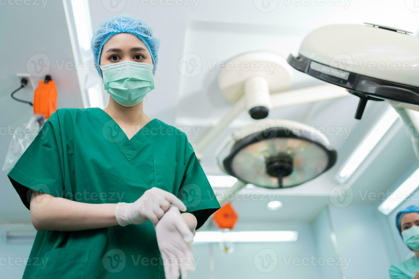 Porträt eines asiatischen Chirurgen mit medizinischer Maske, der im Operationssaal eines Krankenhauses medizinische Handschuhe trägt. Team von professionellen Chirurgen. gesundheitswesen, rettungsdienstkonzept foto