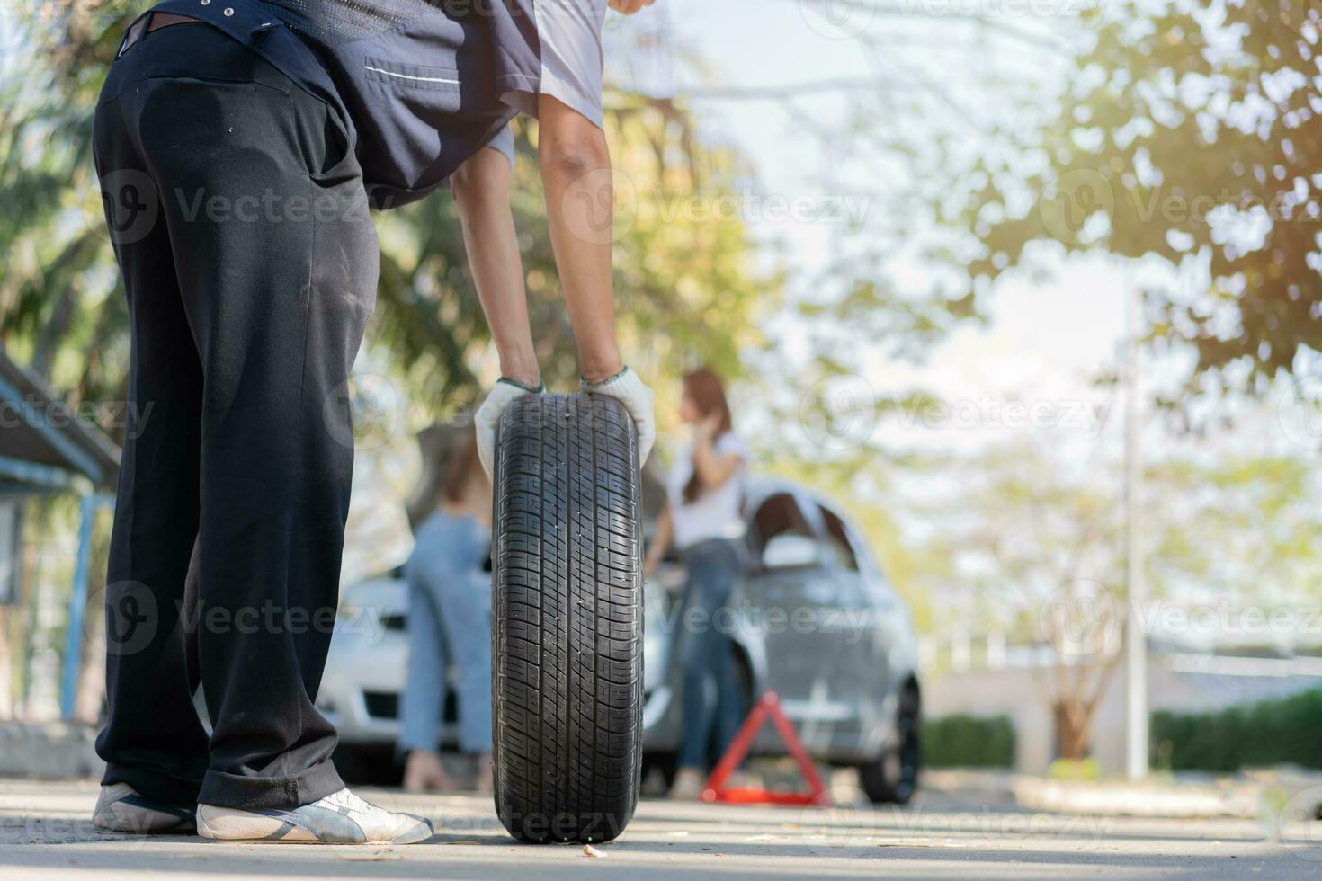 Sachverständiger Mechaniker in Uniform, der einen Reifen hält, um einer Frau beim Radwechsel auf der Autobahn zu helfen, Autoservice, Reparatur, Wartungskonzept. foto