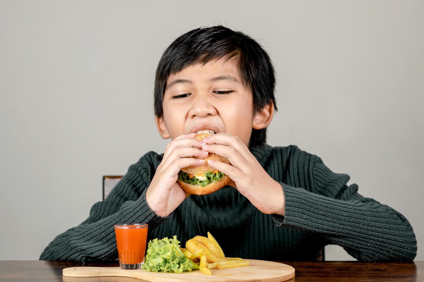 süßer asiatischer Junge, der mit Glück einen leckeren Hamburger isst foto