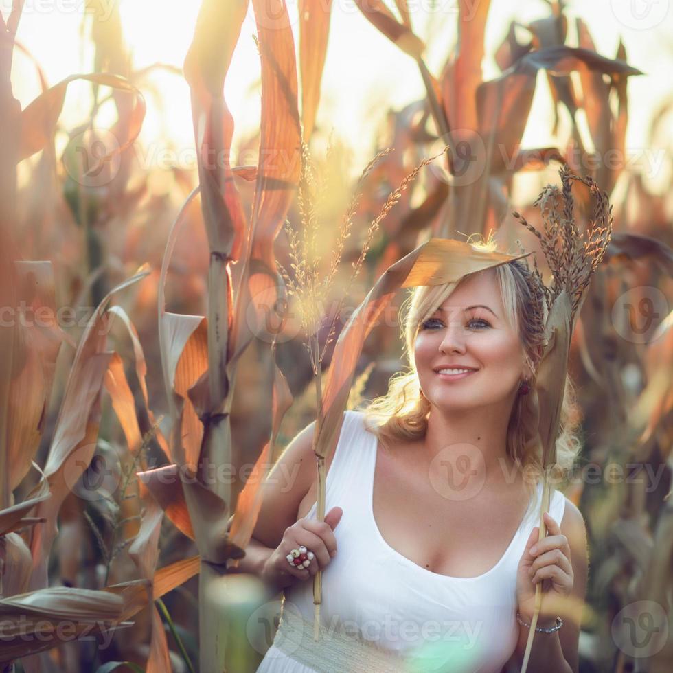 Frau in einem langen weißen Sommerkleid geht auf einem Maisfeld und posiert in der Sonnenuntergangszeit. foto