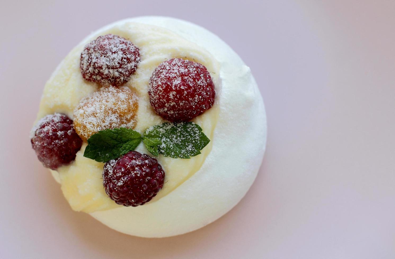 weißer Baiserkuchen mit gelben und roten Himbeeren auf rosa Teller Platz für Text foto