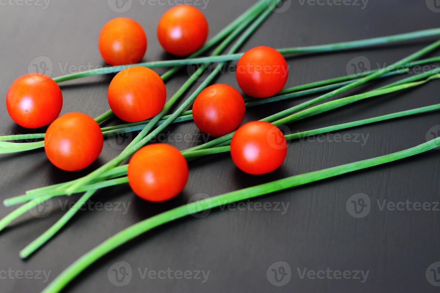 kleine rote Kirschtomaten und frische Frühlingszwiebeln auf rustikalem schwarzem Hintergrund, Draufsicht, Kopienraum foto