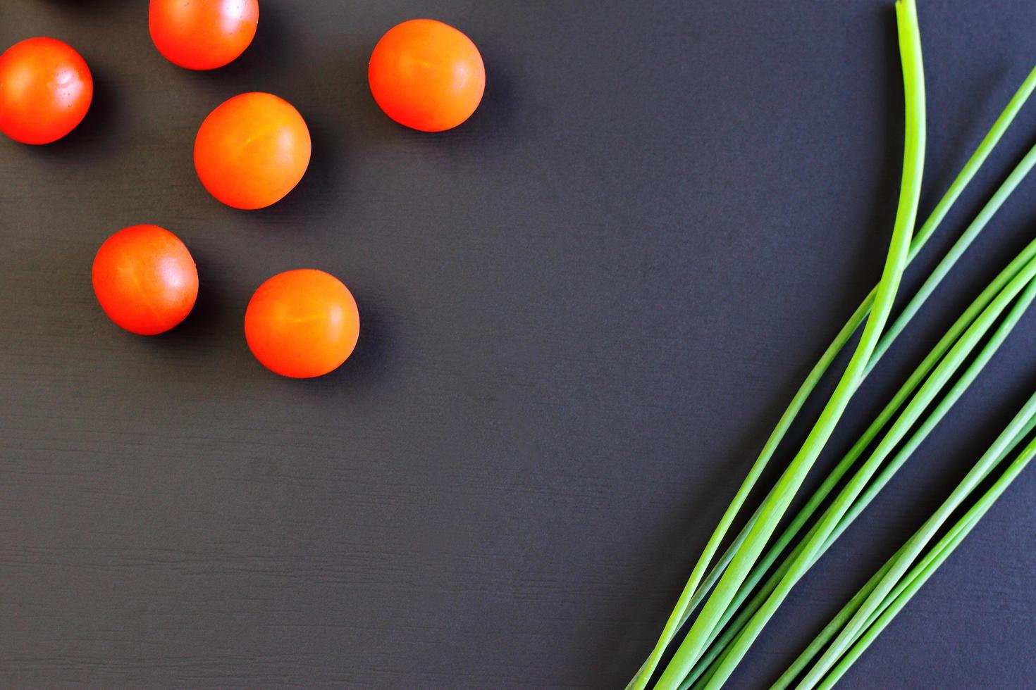 kleine rote Kirschtomaten und frische Frühlingszwiebeln auf rustikalem schwarzem Hintergrund, Draufsicht, Kopienraum foto