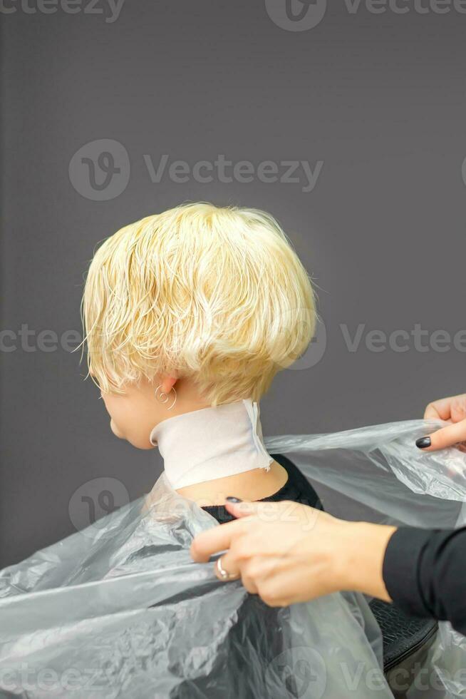 Friseur Abdeckungen Hals mit Kap zum ein weiblich Klient im ein Schönheit Salon. foto