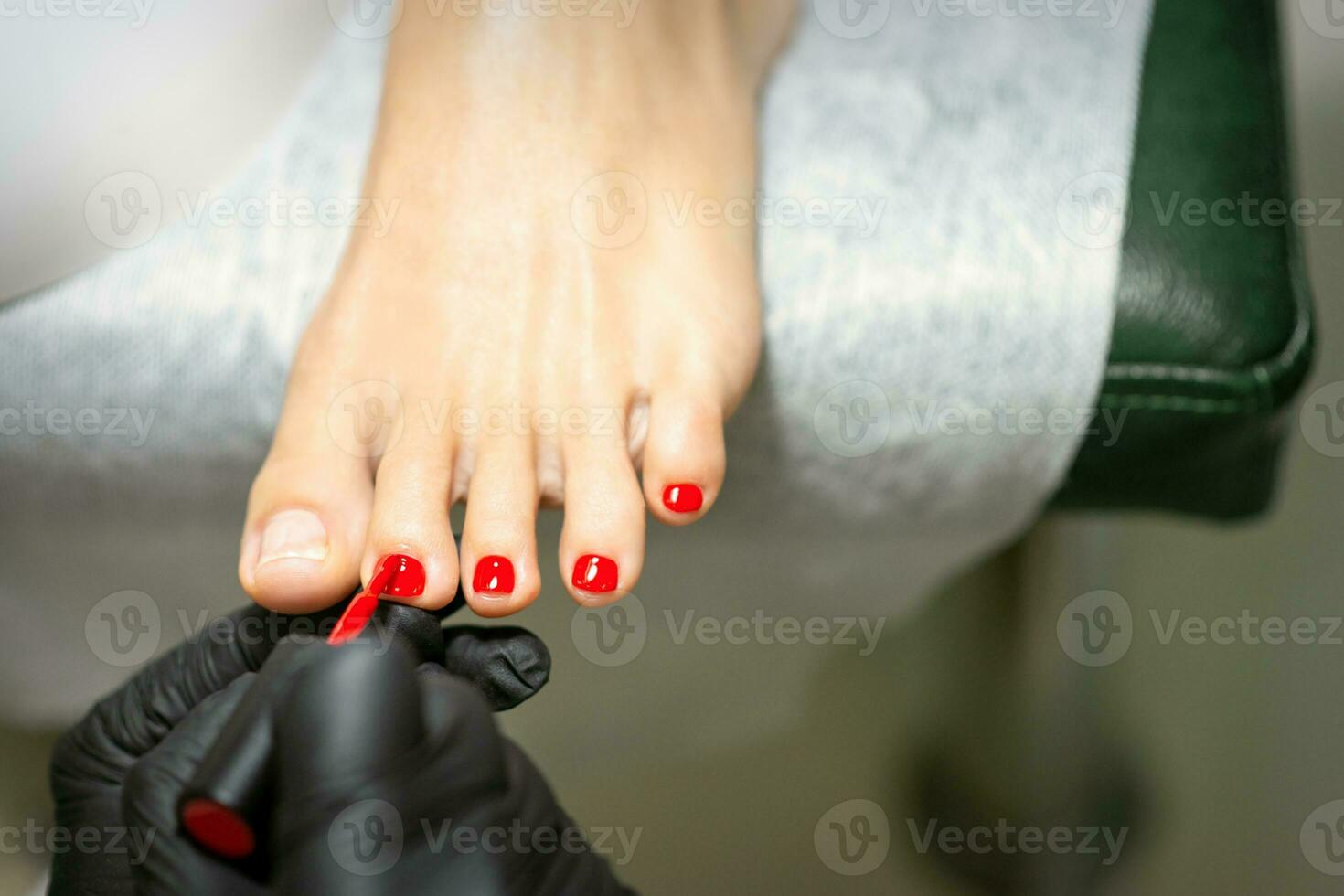 Fußpfleger bewirbt sich rot Nagel Polieren zu das weiblich Zehennägel im ein Schönheit Salon. foto