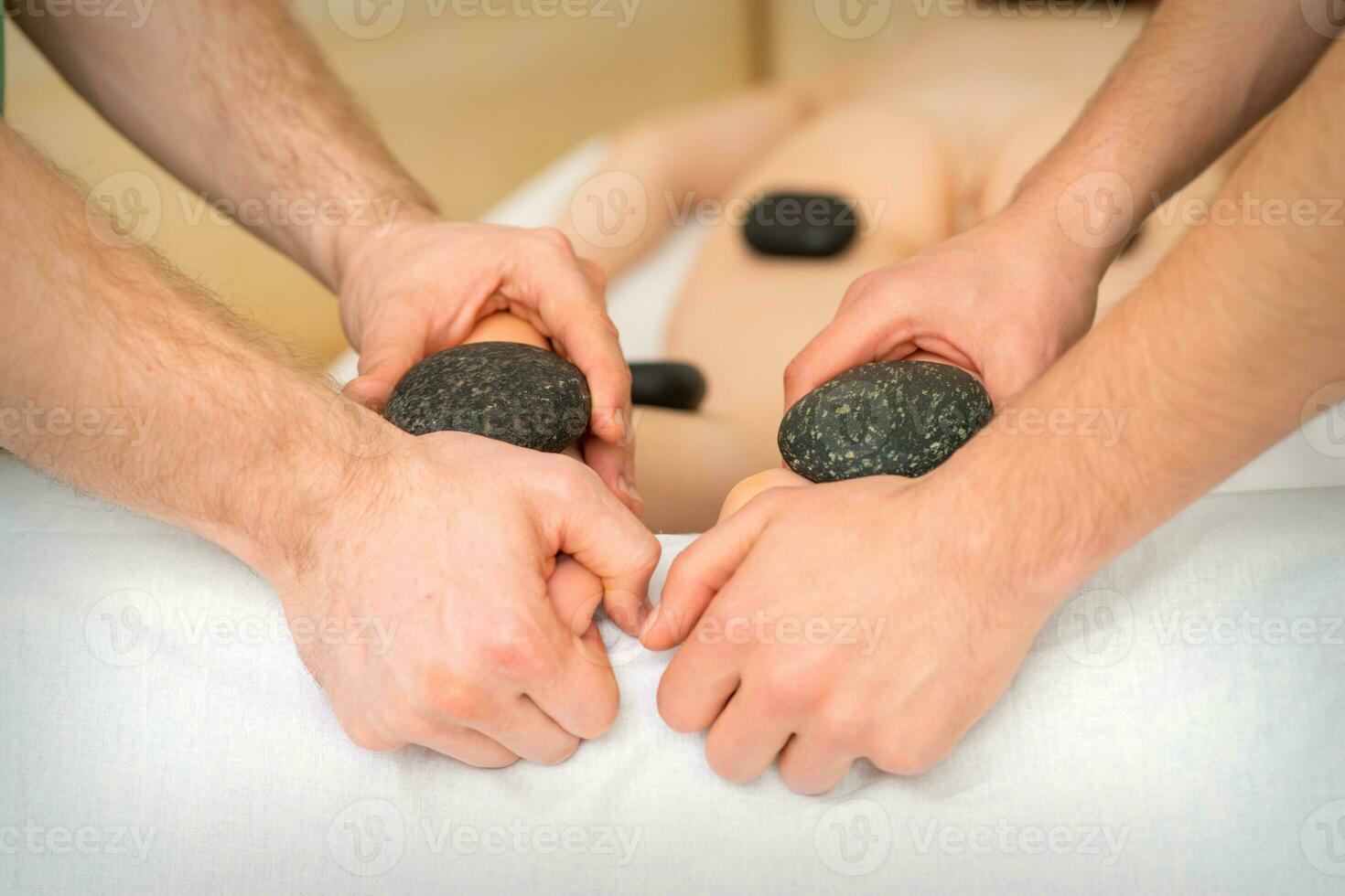 zwei Masseure machen ein Fuß Massage mit ein heiß Stein im vier Hände beim das Spa. foto