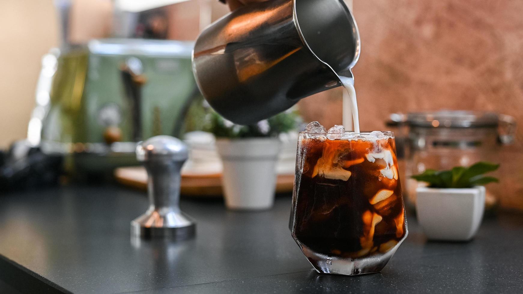 Barista gießt Milch in ein Glas Eiskaffee foto