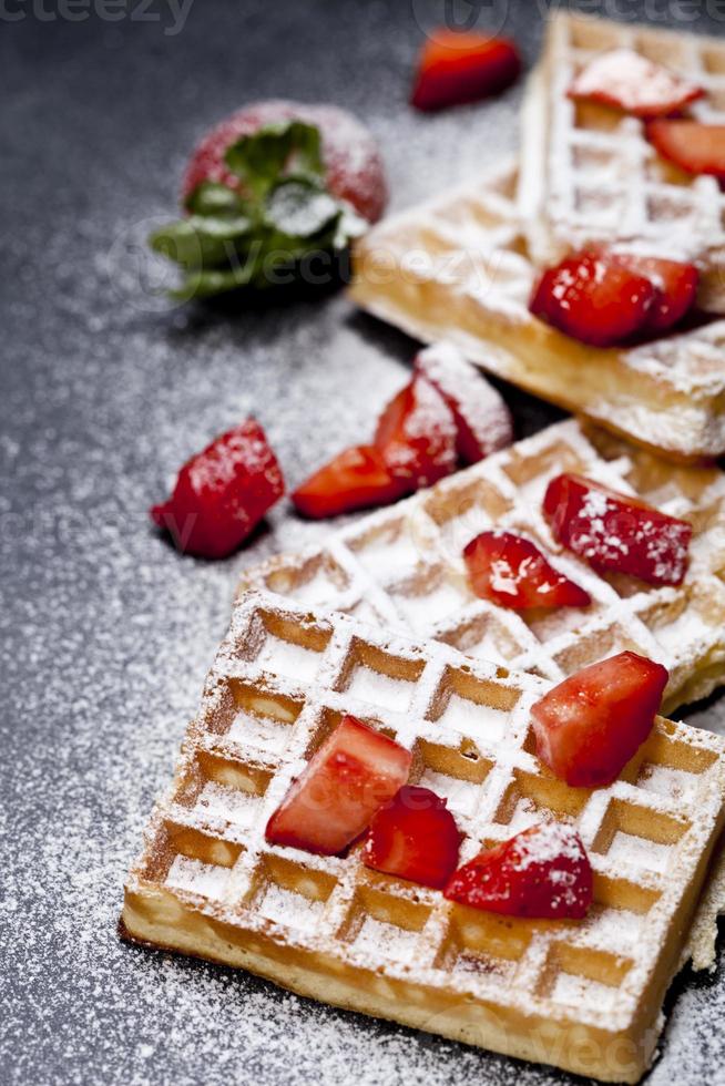 belgische Waffeln mit Erdbeeren und Zuckerpulver auf schwarzem Bretthintergrund. foto