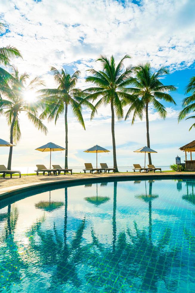 Wunderschöner Luxus-Sonnenschirm und -Stuhl um den Außenpool im Hotel und Resort mit Kokospalme am blauen Himmel foto