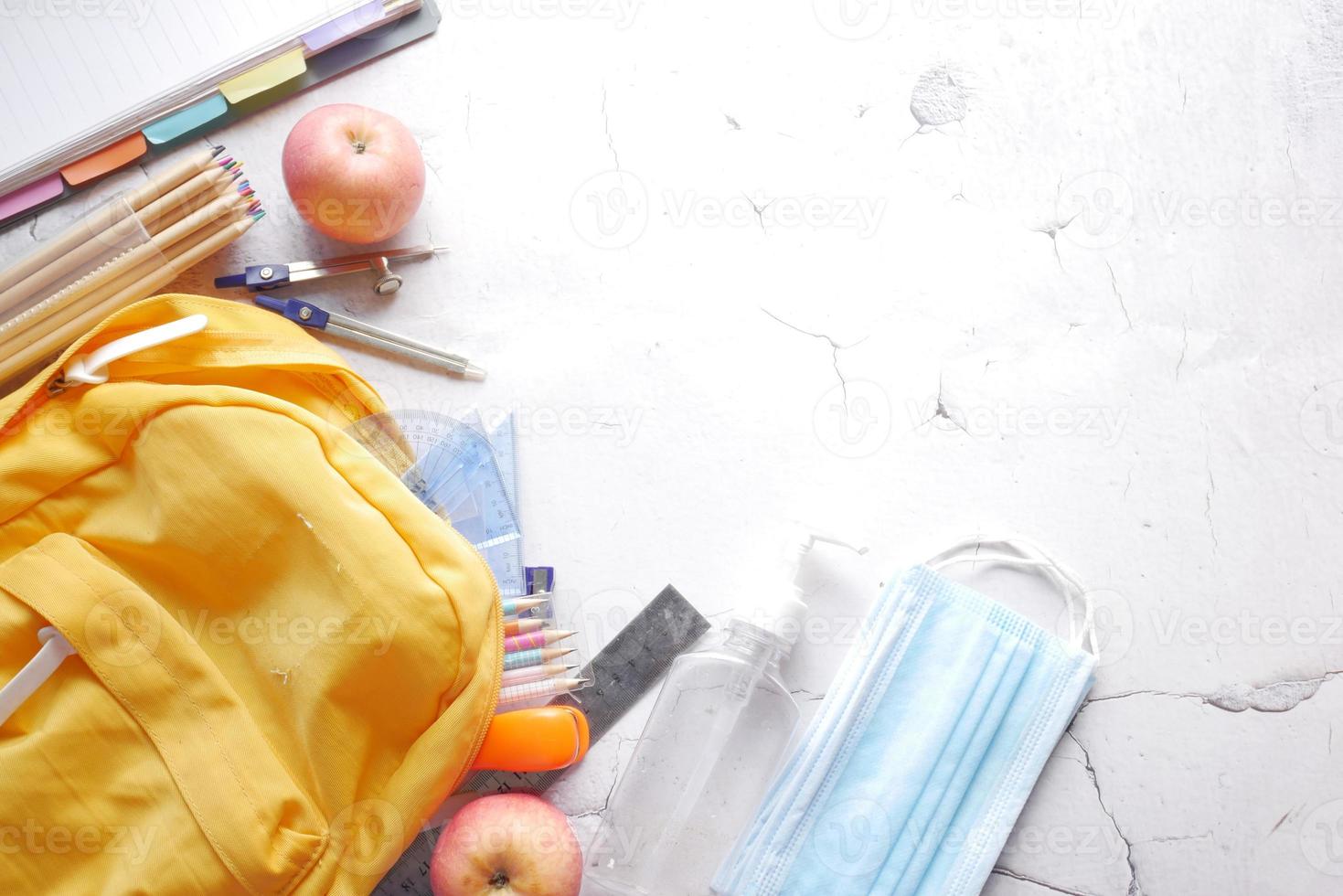 Schultaschenpackung für Schüler mit Desinfektionsmittel, eine Gesichtsmaske auf dem Tisch foto