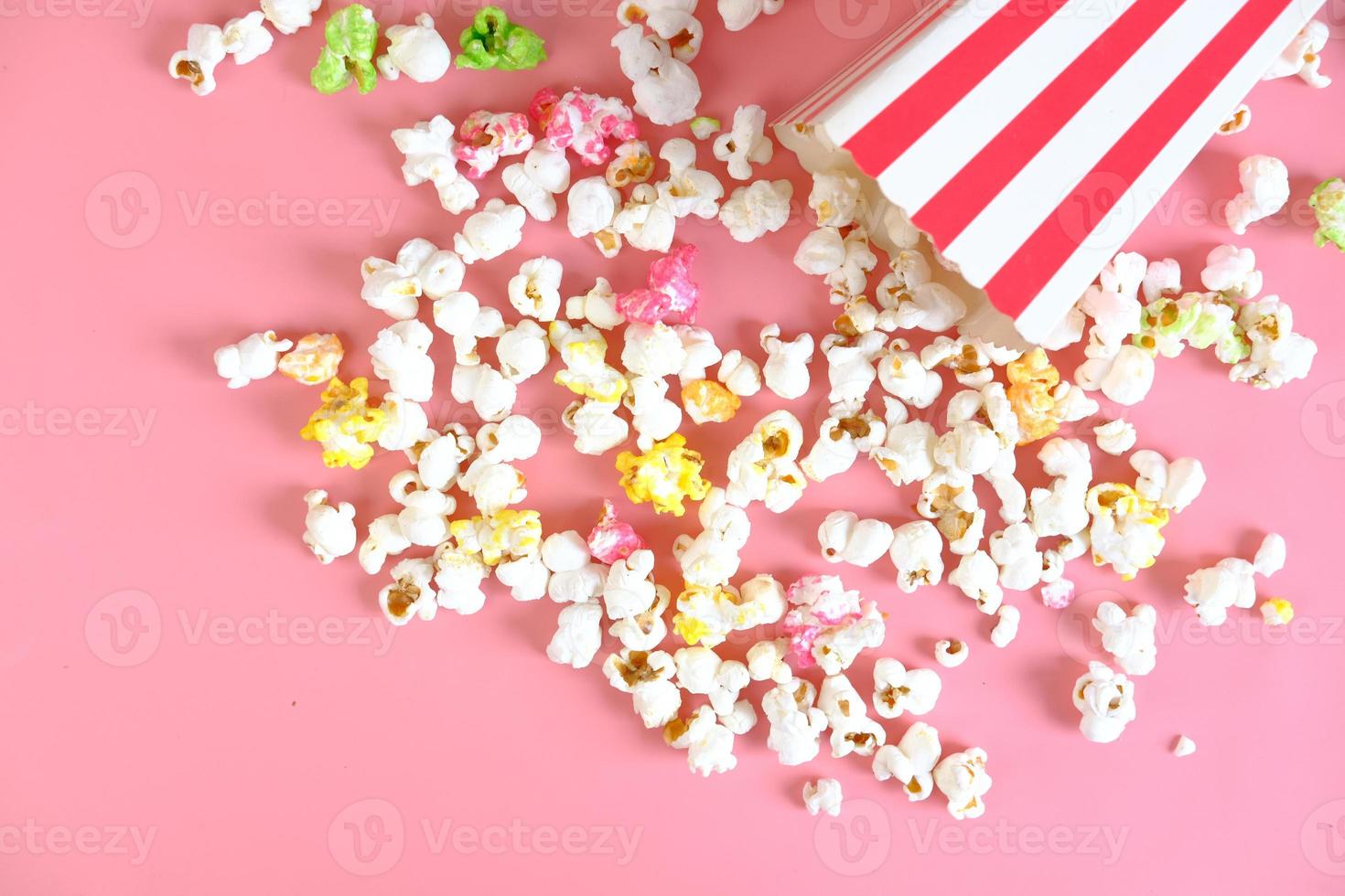 Popcorn verschüttet aus einem Behälter auf rosa Hintergrund foto