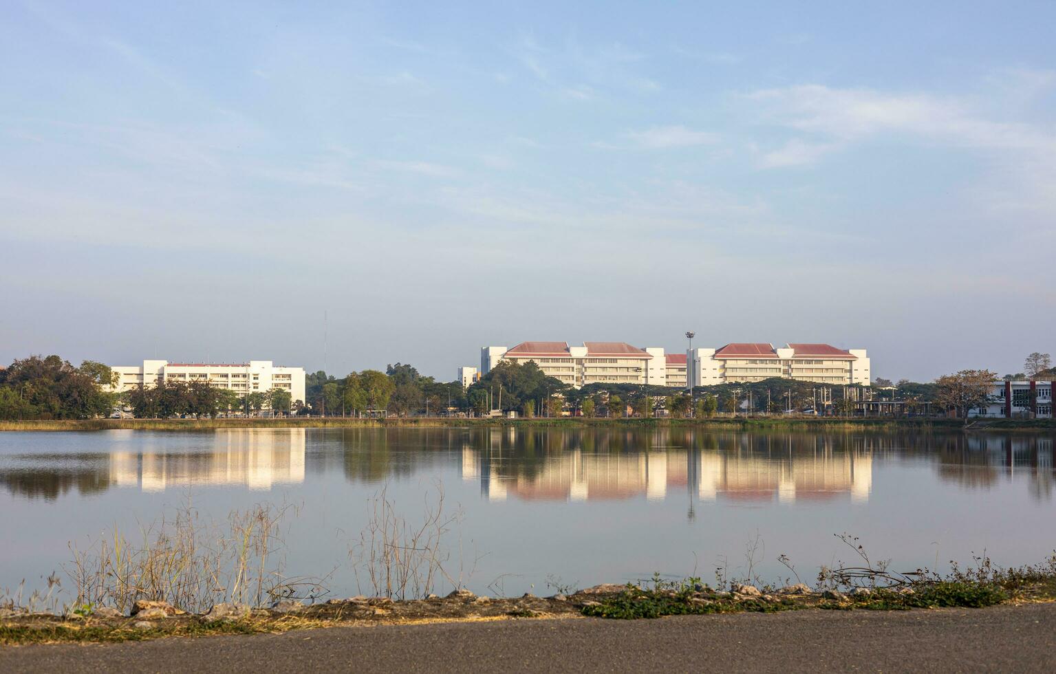 Panorama- Aussicht von Gebäude in der Nähe von Bäume Nächster zu das Ufer von ein groß Teich mit Wasser Reflexionen. foto