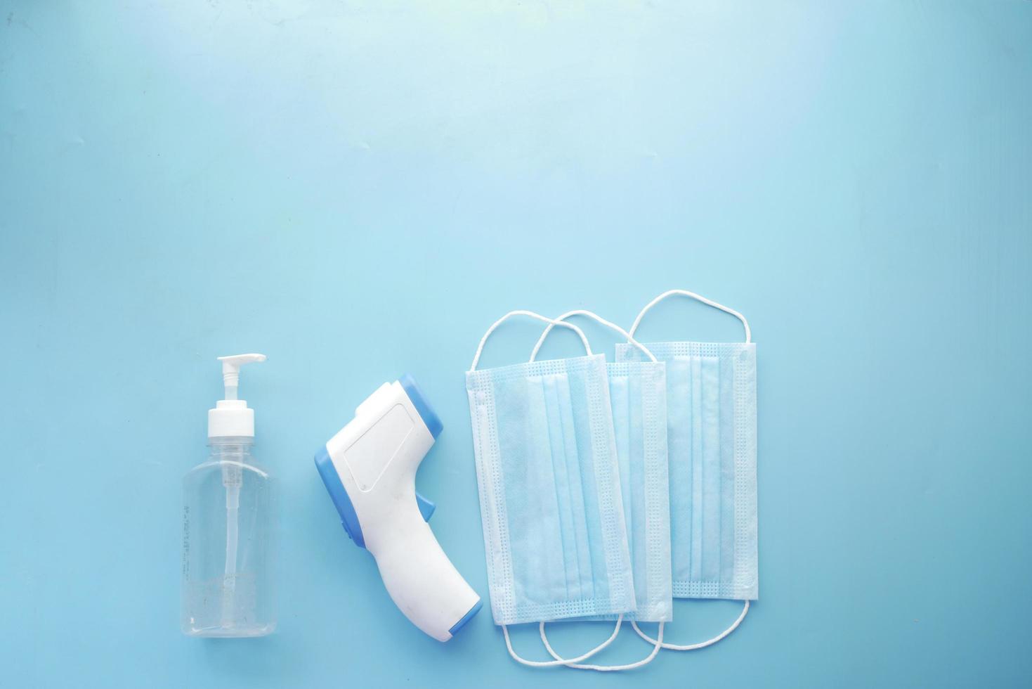 Operationsmasken, Thermometer und Händedesinfektionsmittel auf blauem Hintergrund foto