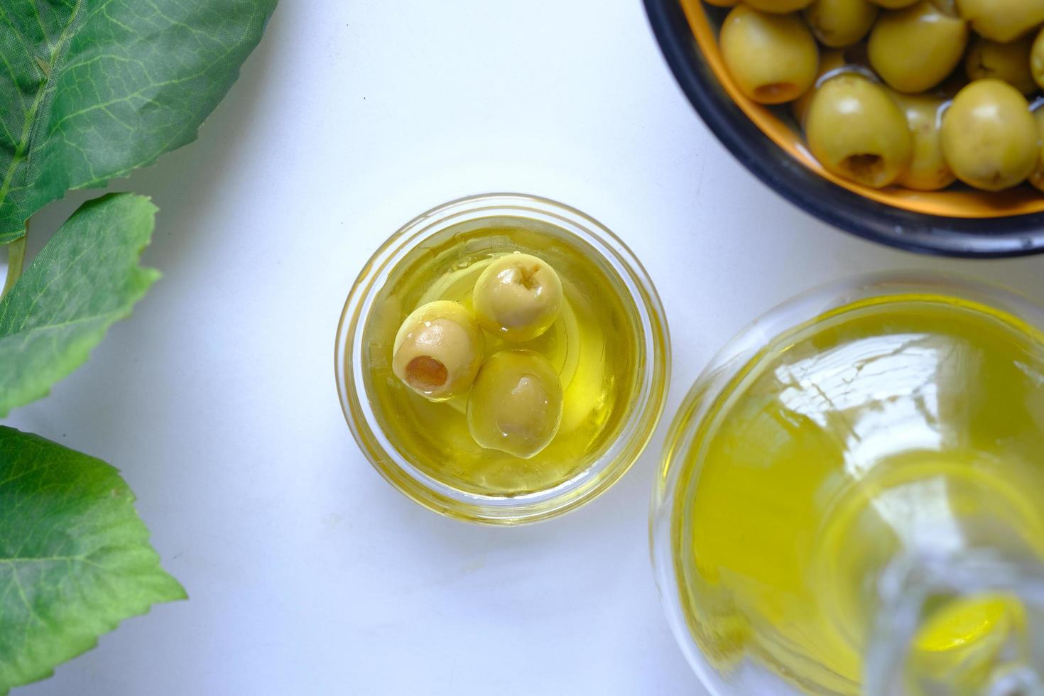 Flasche Olivenöl und frische Oliven in einem Behälter auf weißem Hintergrund foto