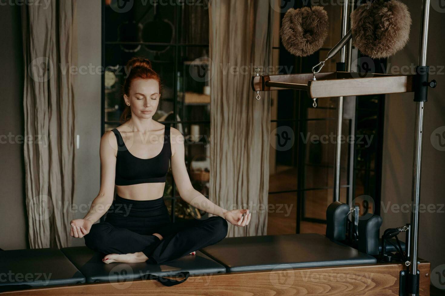 friedlich weiblich Pilates Lehrer sitzt im Yoga Lotus auf Cadillac Reformer, suchen Entspannung nach heftig Dehnen im das Studio. Umarmen Meditation und Yoga Konzept. foto