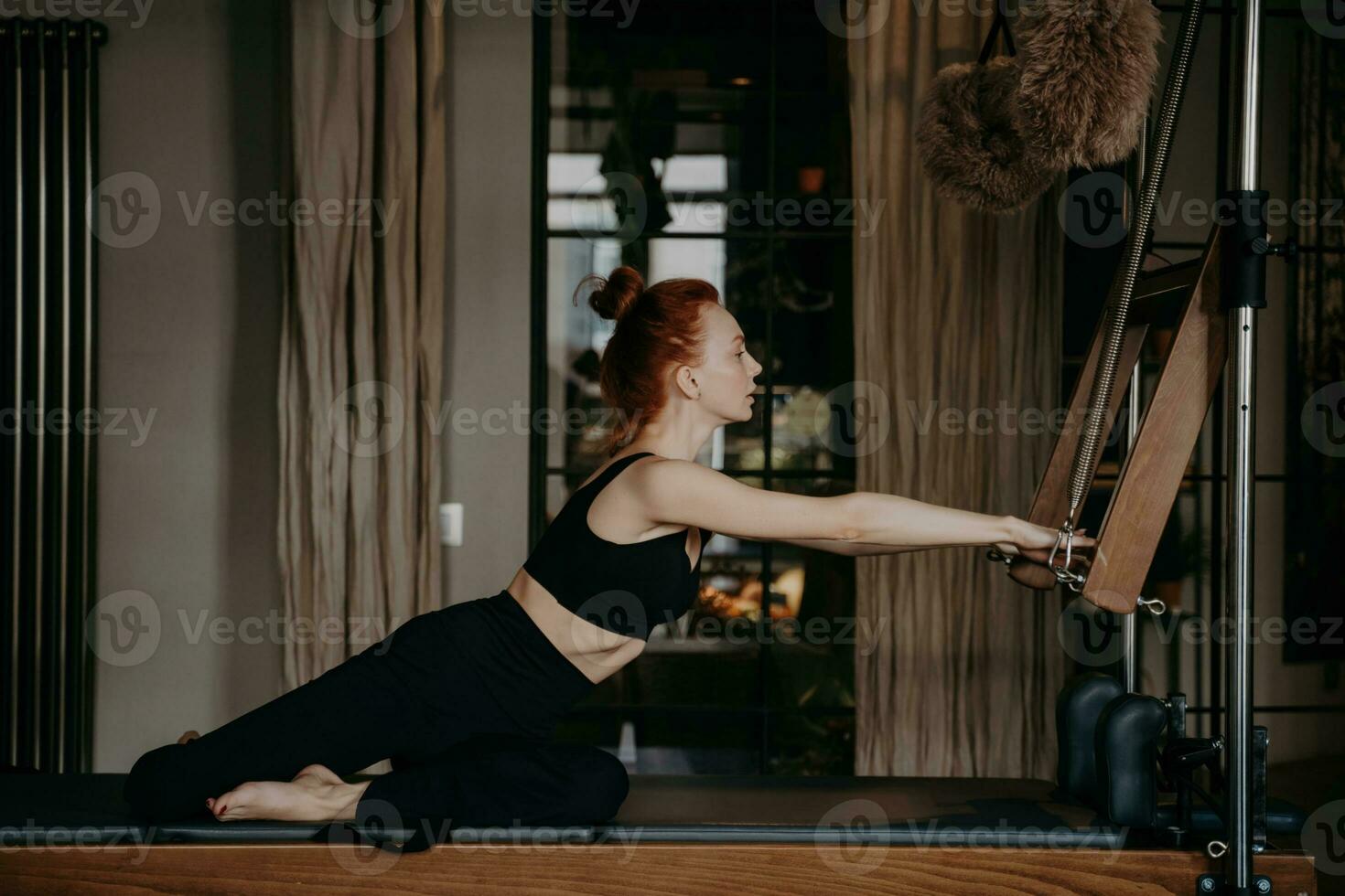 rothaarig Pilates Lehrer im Sportbekleidung Vitrinen sportlich Körper auf Cadillac Reformer, demonstrieren Dehnen im Fitnessstudio. foto