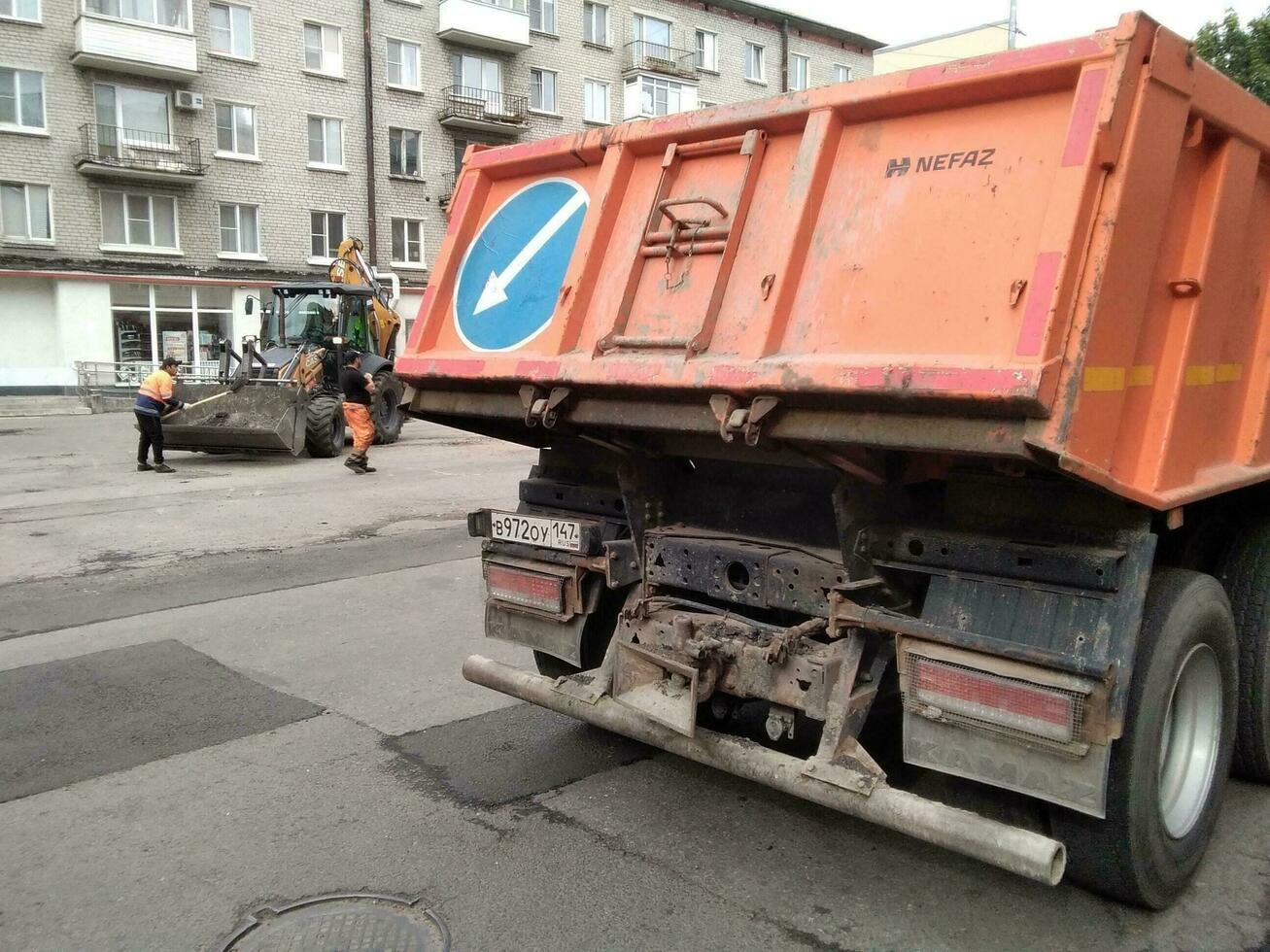 sankt Petersburg Russland - - 07 31 2023 Konstruktion Arbeit auf das Anordnung von das Hof und Umgebung Bereiche, ein Arbeiter Sägen ein Stück von Beton Block. das zweite Arbeiter Spaziergänge mit ein Schaufel. foto