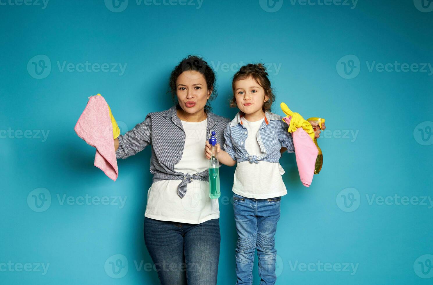 Frau und Mädchen mit Reinigung liefert im das Hände posieren beim Kamera ausdrücken Unzufriedenheit mit Reinigung. Mama und Tochter. Blau Hintergrund mit. Kopieren Raum. foto