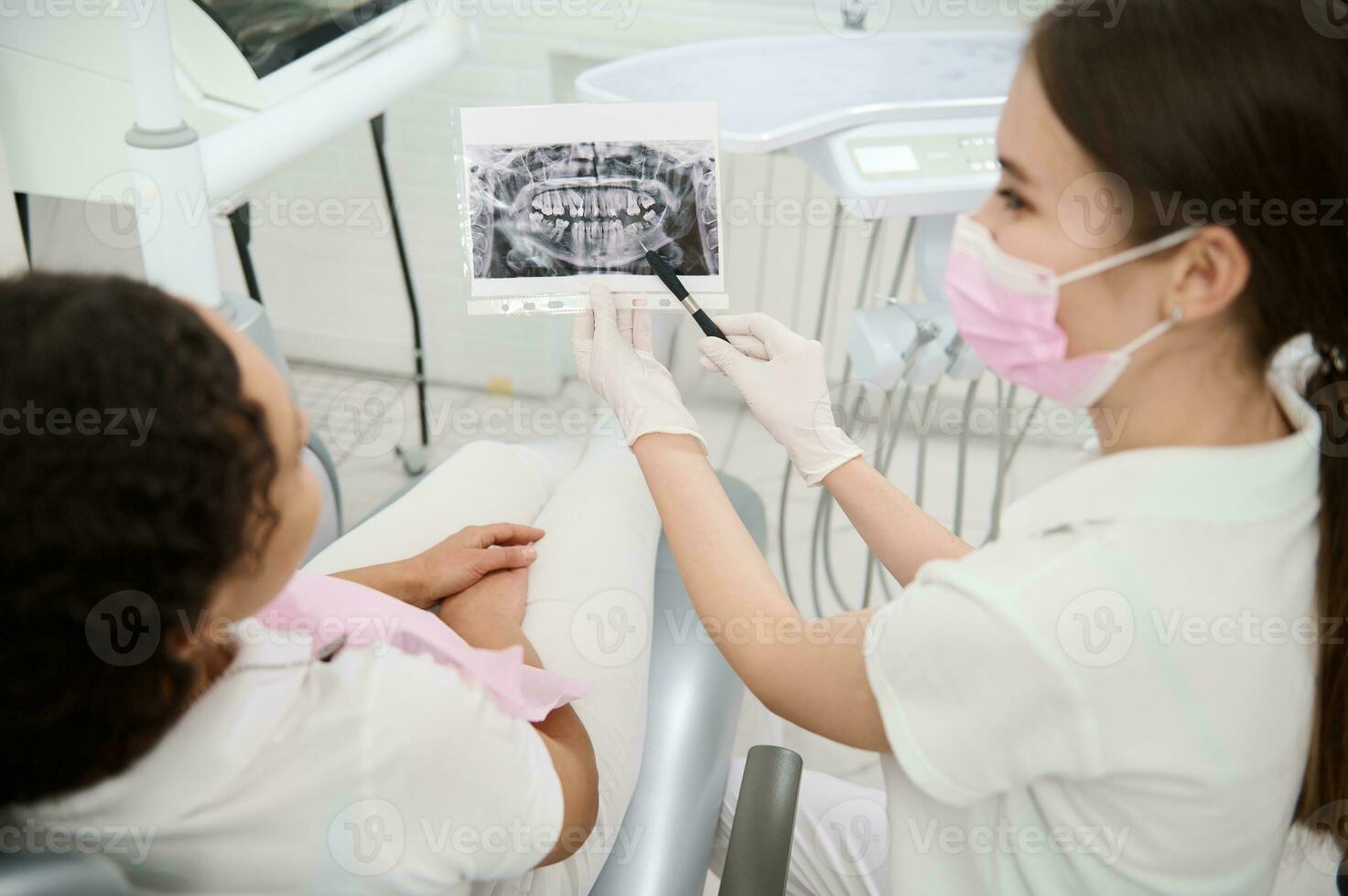 Fokus auf Dental Röntgen im das Hände von ein weiblich Zahnarzt erklären das Behandlung zu geduldig Sitzung im Zahnärzte Stuhl während geplanter Termin im medizinisch Klinik. Konzept von medizinisch Diagnose im Zahnheilkunde. foto