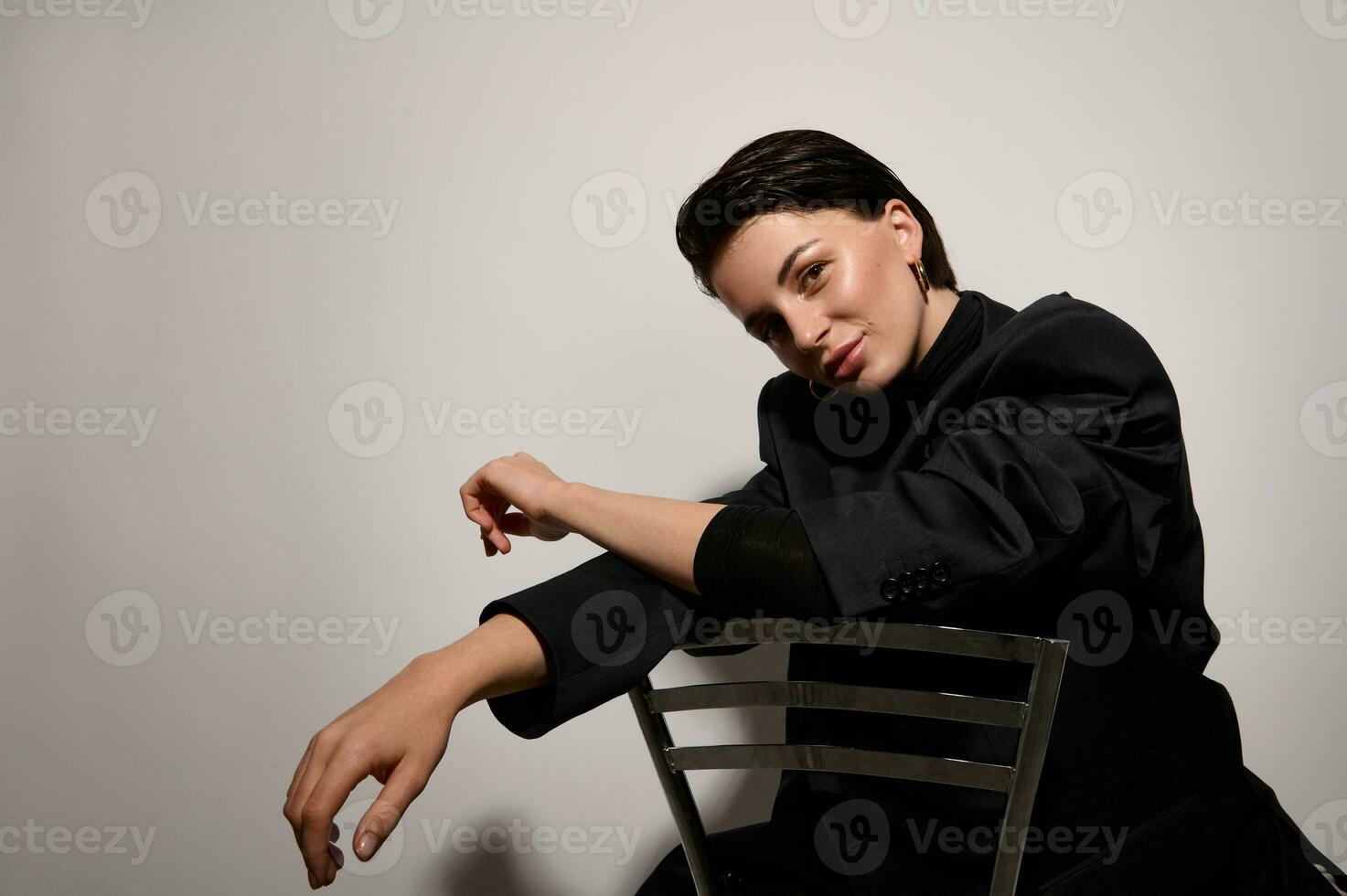 Studio Schuss, horizontal Porträt von schön Herrlich modisch jung Brünette mit gesund glänzend sauber Haut, posieren suchen beim Kamera Sitzung auf ein Stuhl gegen Weiß Hintergrund mit Kopieren Raum foto