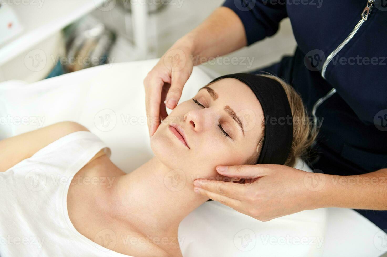 Arzt-Kosmetikerin Hände massieren das Gesicht von entspannt jung Frau. Gesicht Heben Antialterung Massage. Fachmann lymphatisch Drainage Massage beim Spa Klinik foto