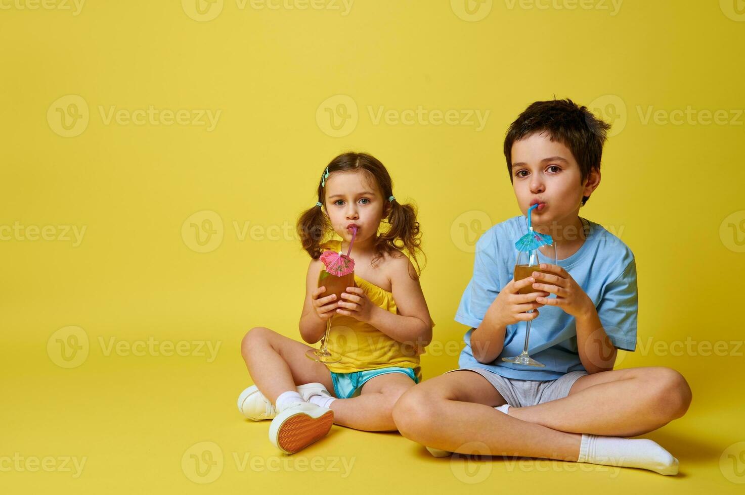 süß Kinder, Junge und Mädchen Trinken von ein Stroh ein köstlich Cocktail, posieren Über Gelb Hintergrund. Kopieren Raum foto