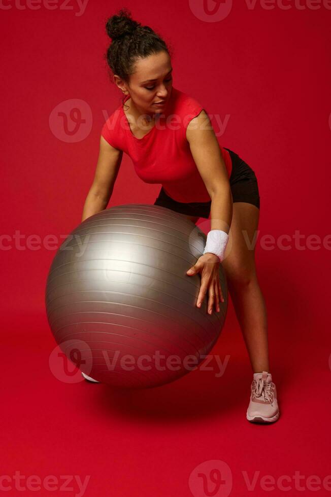 Mitte alt multiethnisch sportlich Frau ausüben mit Fitness Ball gegen rot Hintergrund mit Kopieren Anzeige Raum zum Werbung Text foto