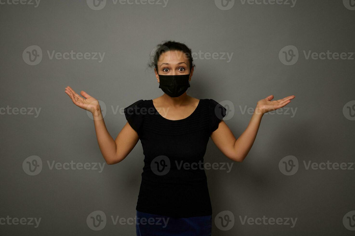 isoliert Porträt auf grau Hintergrund von ein erstaunt Frau im schwarz schützend medizinisch Maske erziehen ihr Hände Palmen hoch, halten ein imaginär Kopieren Raum zum Werbung. schwarz Freitag Konzept foto