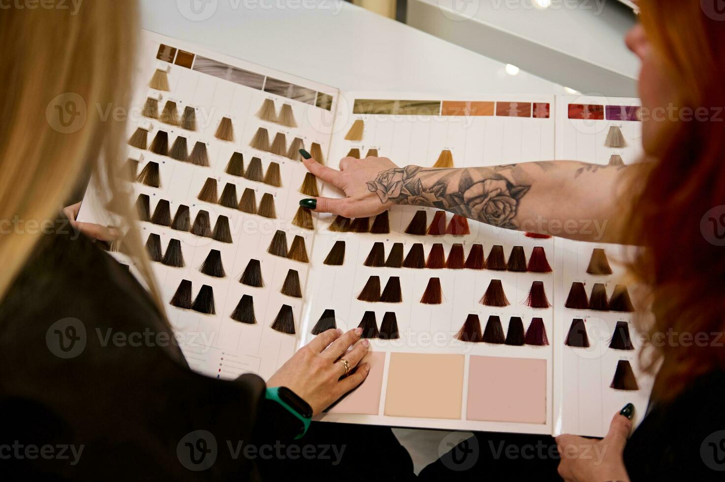 Overhead Aussicht zu ein Rothaarige weiblich Haar Stylist tätowiert Hand, auf ein Katalog von Haar Farbstoff Farbe Diagramm Palette und Beratung Kunde, Haar Salon Klient zu wählen das Farbe. Fachmann Haar Sterben Konzept foto