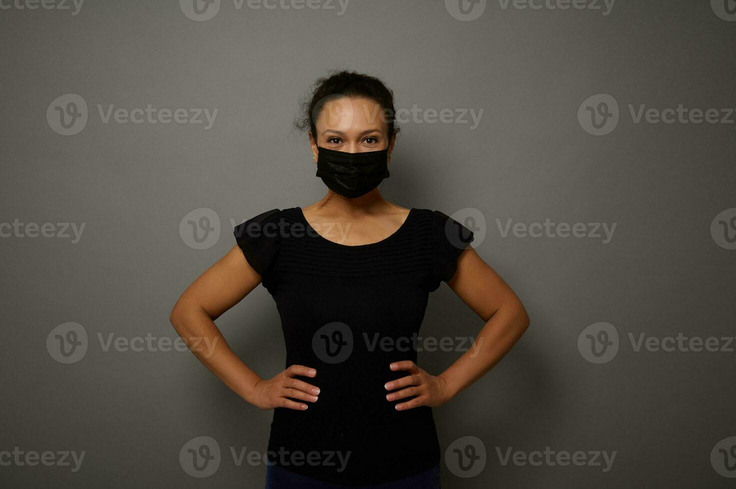 isoliert Porträt auf grau Hintergrund von ein Frau im schwarz medizinisch schützend Maske suchen beim Kamera mit Hände auf Taille. Kopieren Raum zum Werbung. schwarz Freitag Konzept foto
