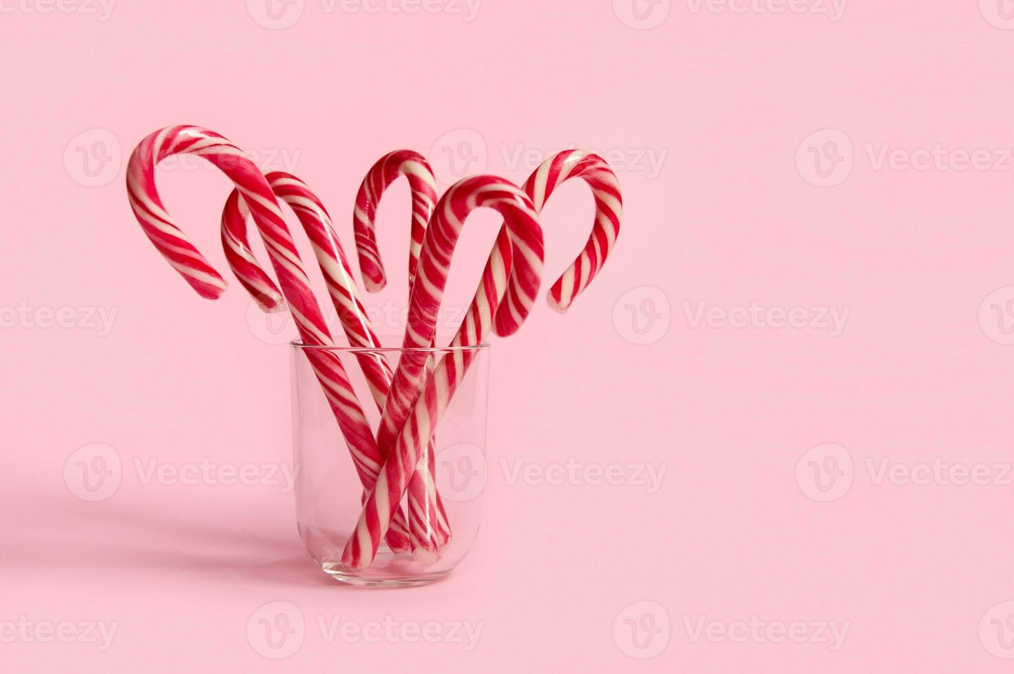 schön minimalistisch einfach Komposition mit Weihnachten Lutscher auf transparent Glas auf Rosa farbig Hintergrund mit Kopieren Raum zum Weihnachten Anzeige foto